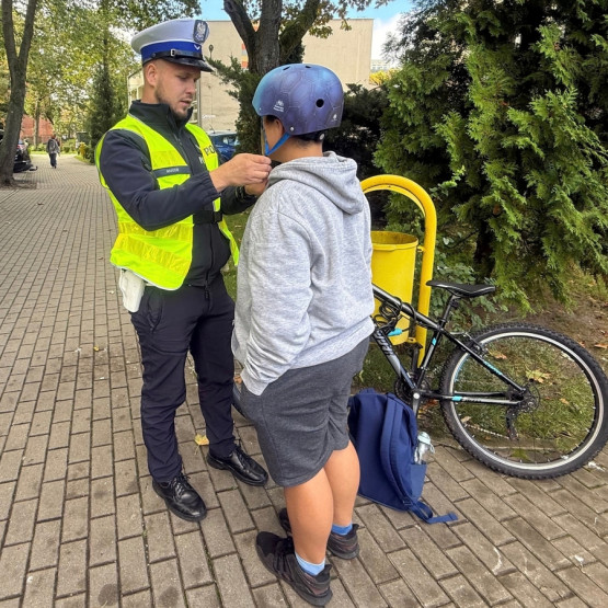 Policjant pomaga dziecku prawidłowo zapiąć kask rowerowy podczas działań profilaktycznych. Źródło zdjęcia: ksp.policja.gov.pl.